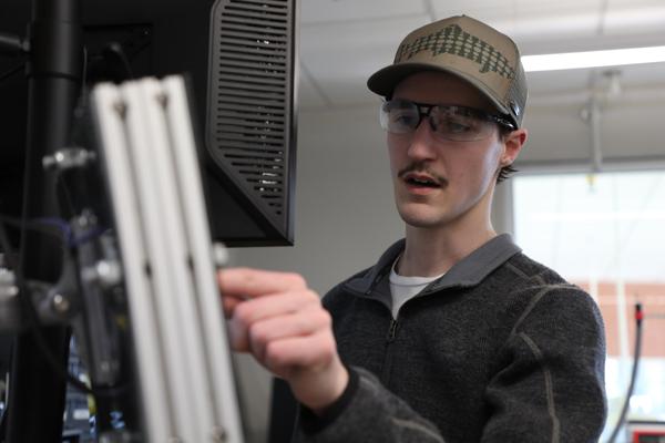Student wearing safety glasses pointing at a computer monitor